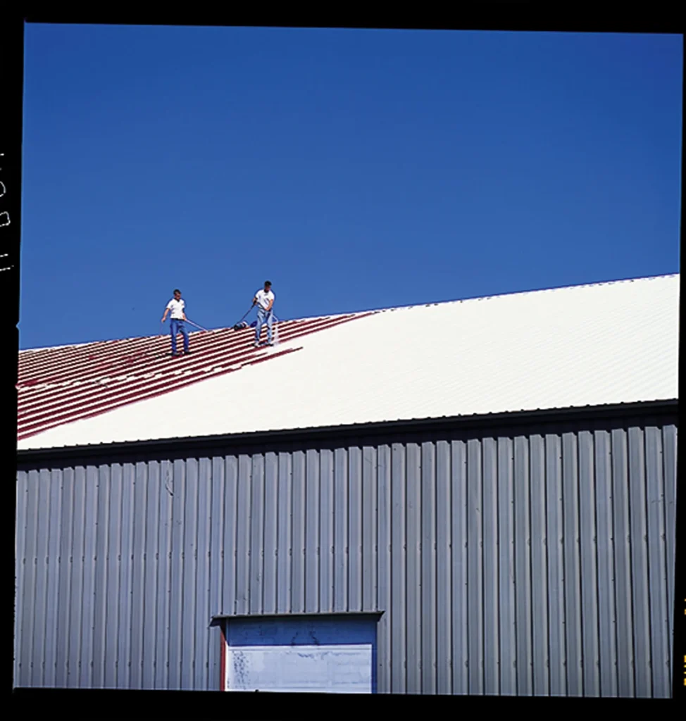 Metal building roof partway through a white restoration coating