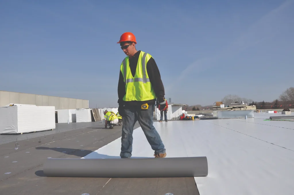 Roofer rolling out single ply membrane on a commercial roof
